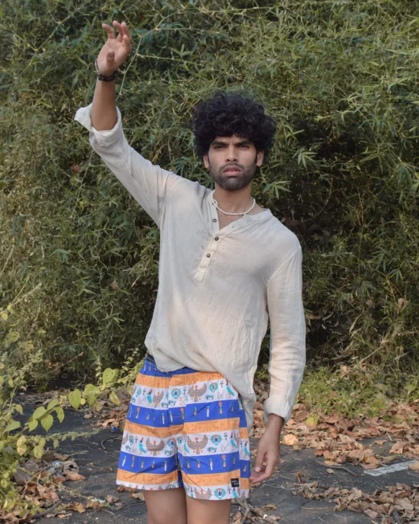 Man in a beige kurta and Whats Down Cleopatra blue-and-orange printed boxers reaching up in the grassland