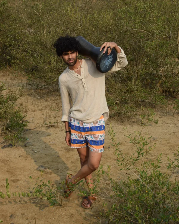 Man in a beige kurta and Whats Down Cleopatra blue-and-orange printed boxers on a dirt path with a drum