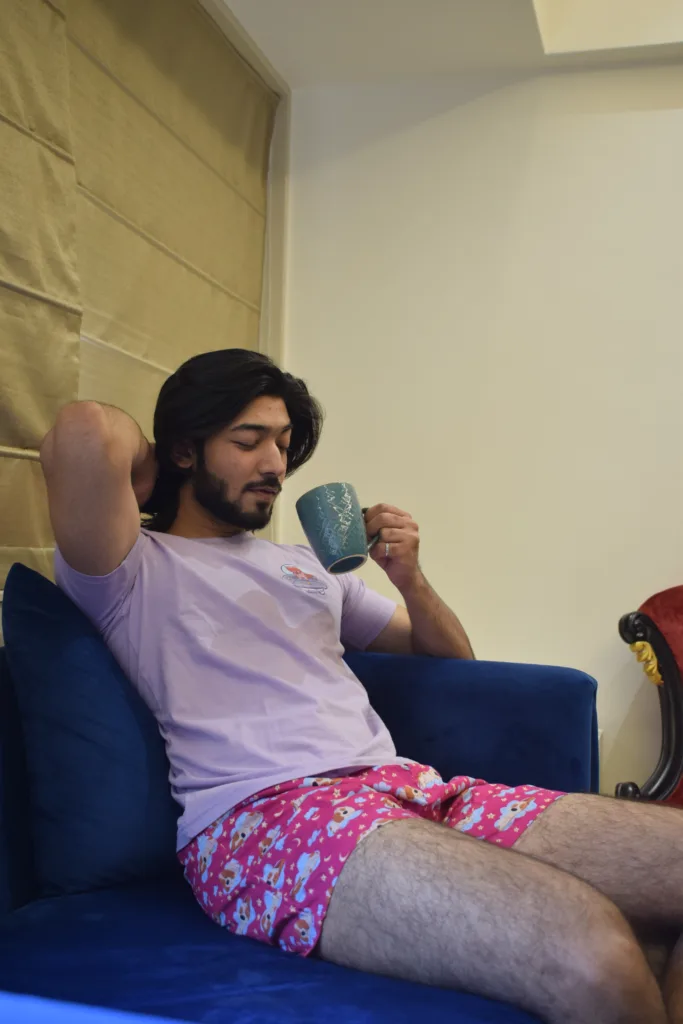 Man in a pink tee and Whats Down pink printed boxers on a sofa with a mug