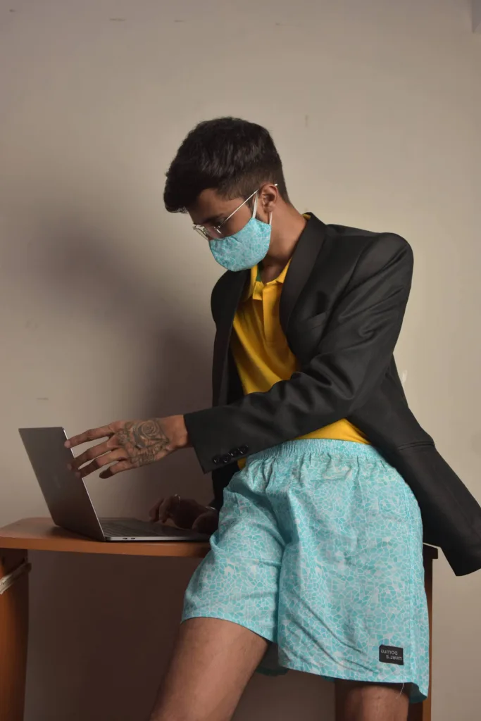 Man in a blazer, Whats Down printed face mask and light-blue printed boxers working on a laptop