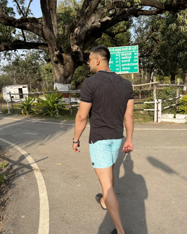 Man in a black tee and Whats Down light-blue printed boxers on a tree-lined road walking away
