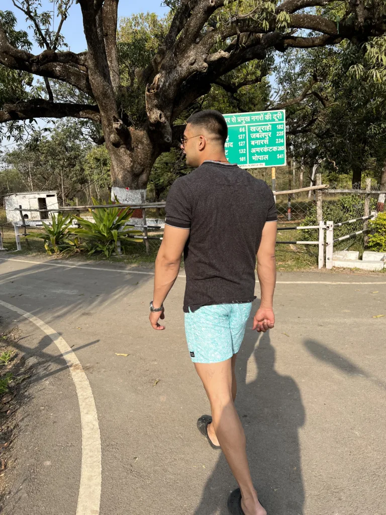 Man in a black tee and Whats Down light-blue printed boxers on a tree-lined road walking away