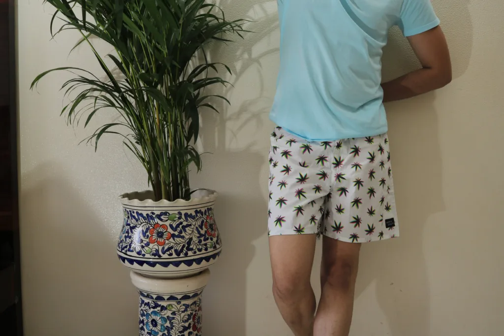 Man in a light-blue tee and Whats Down white printed boxers beside a palm plant. Waistband detail