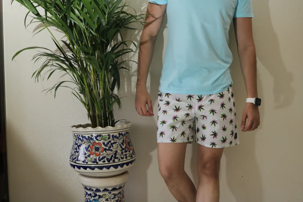 Man in a light-blue tee and Whats Down white printed boxers beside a palm plant. Print detail