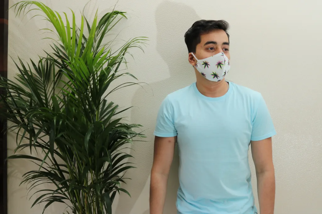 Man in a blue tee and Whats Down printed face mask beside a palm plant