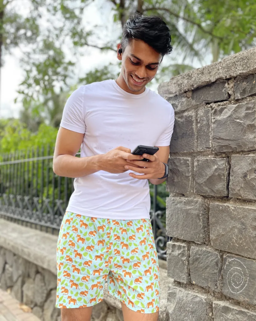 Man in a tee and Whats Down printed cotton boxers checking his phone by an iron gate