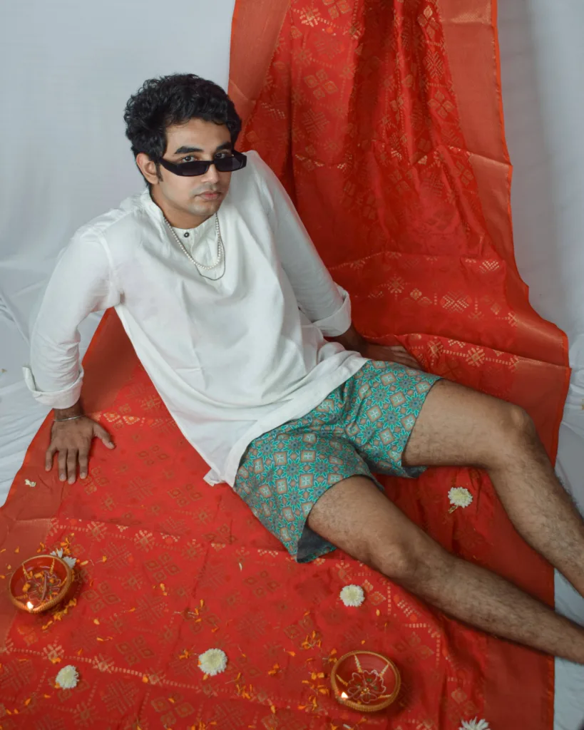 Man in a white sweatshirt, sunglasses and Whats Down green printed boxers on a red drape with marigolds lying back