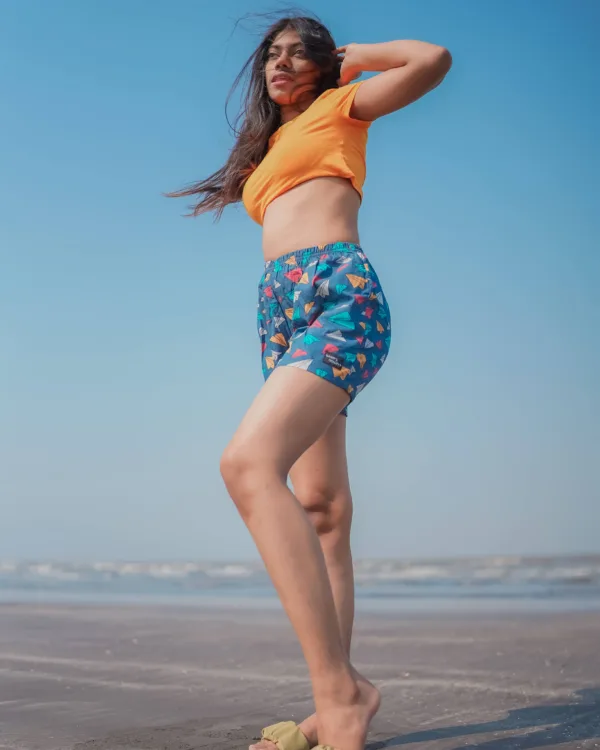 Woman in an orange crop top and Whats Down teal ice-cream printed boxers on the beach arms raised