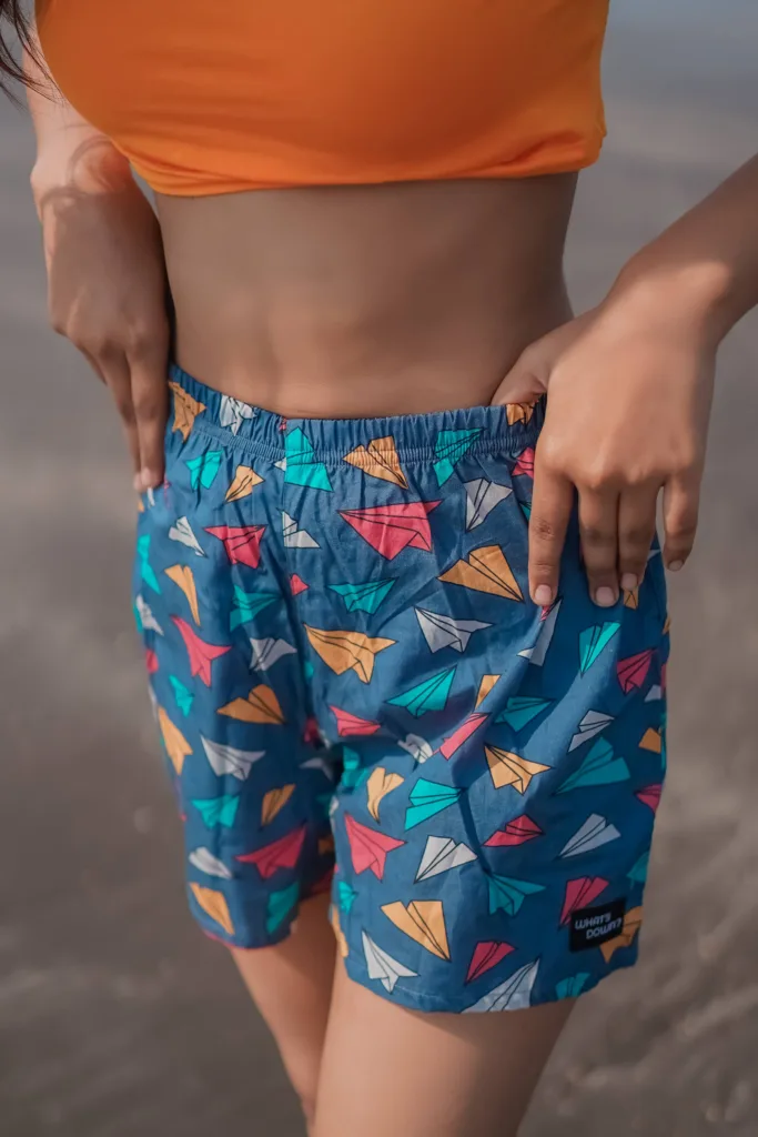Woman in an orange crop top and Whats Down teal ice-cream printed boxers on the beach. Waistband detail