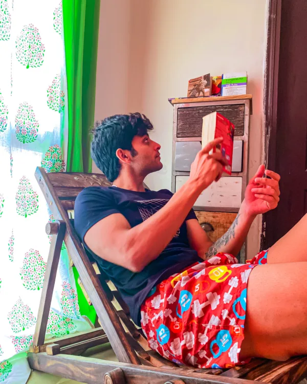 Man in Whats Down red printed boxers on a deck chair by a bright window