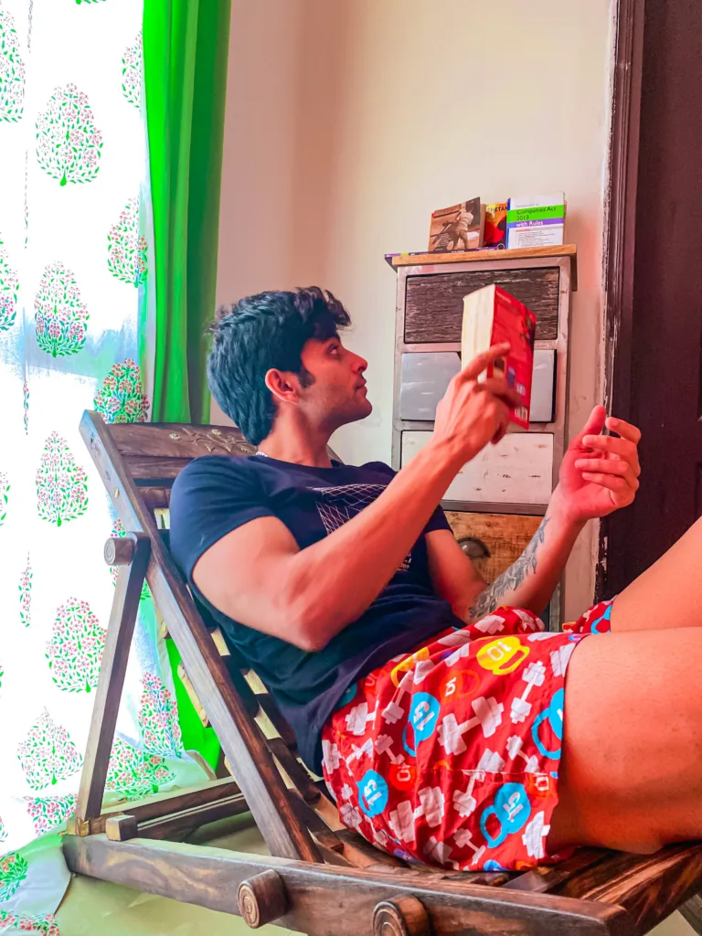 Man in Whats Down red printed boxers on a deck chair by a bright window