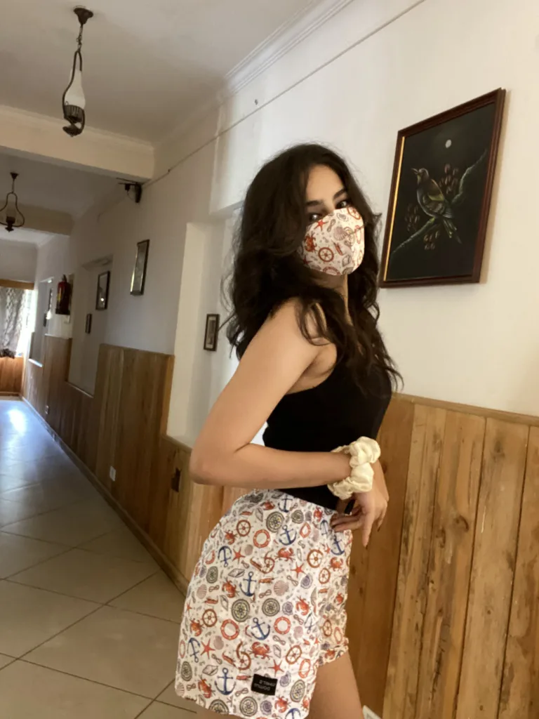 Woman in a Whats Down printed face mask and white floral printed boxers in a hallway