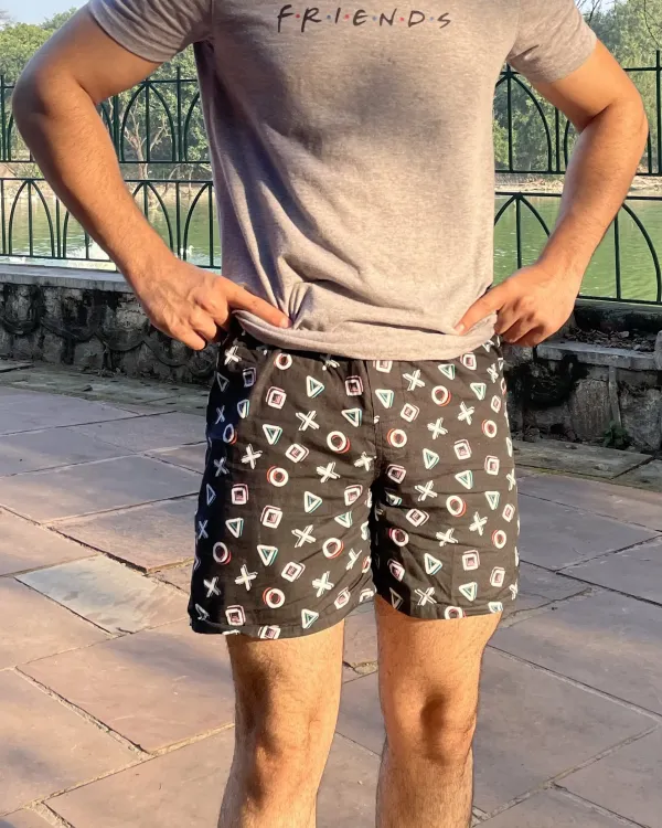 Man in a grey tee and Whats Down black-and-white printed boxers by a lake railing