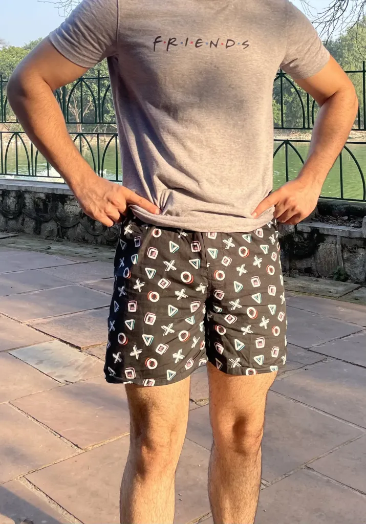 Man in a grey tee and Whats Down black-and-white printed boxers by a lake railing