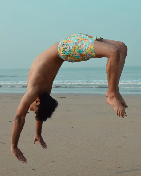 Man in Whats Down yellow-and-blue printed boxers on the beach doing a backflip