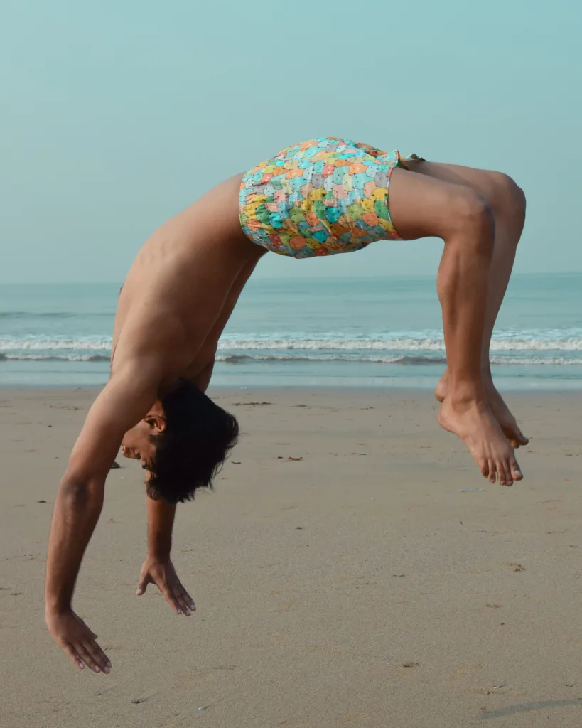 Man in Whats Down yellow-and-blue printed boxers on the beach doing a backflip