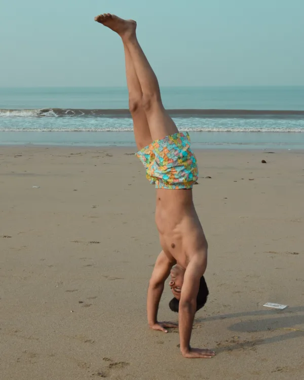 Man in Whats Down yellow-and-blue printed boxers on the beach in a handstand