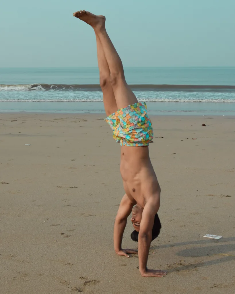 Man in Whats Down yellow-and-blue printed boxers on the beach in a handstand