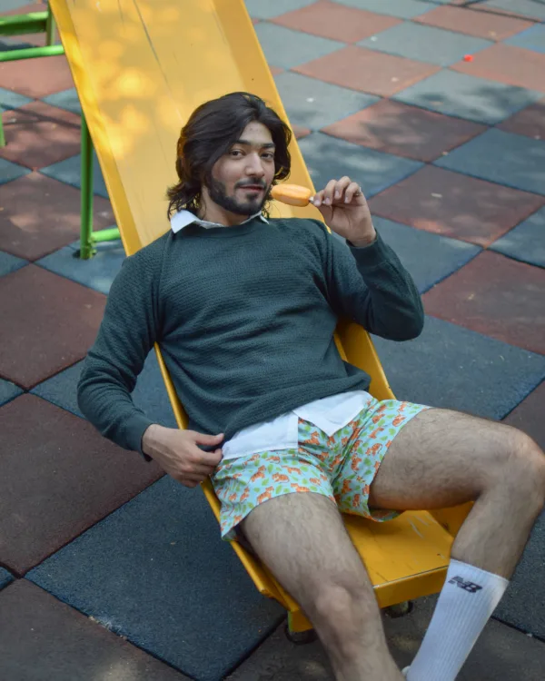Man in a green sweater and Whats Down Green Sher Khan printed boxers at a playground lounging on a slide