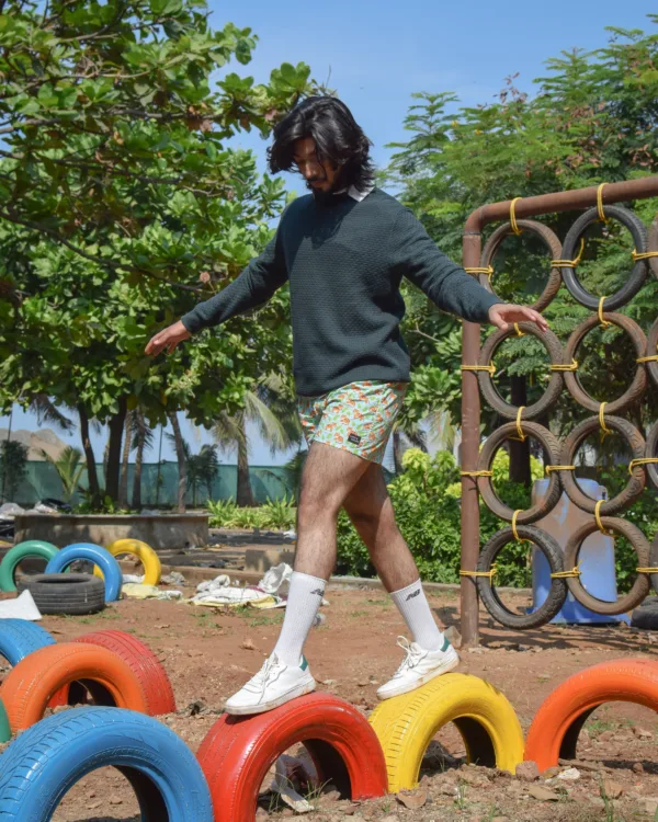 Man in a green sweater and Whats Down Green Sher Khan printed boxers at a playground stepping over tyres