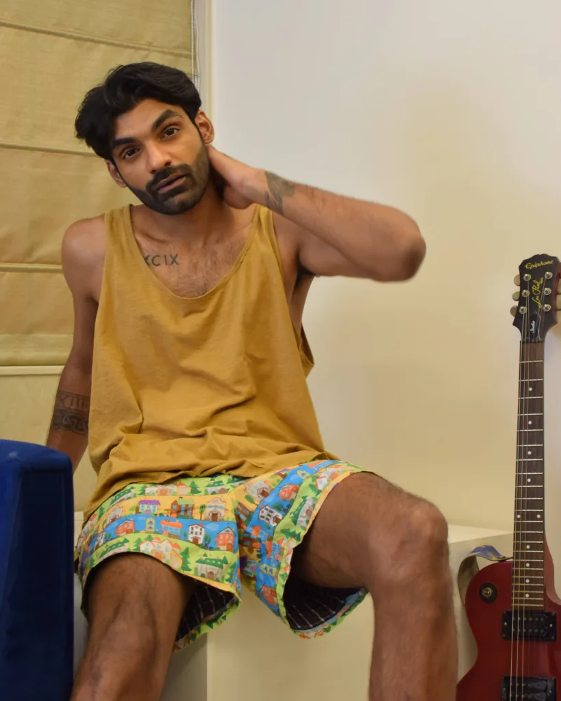 Man in a mustard vest and Whats Down yellow printed boxers sitting beside a guitar