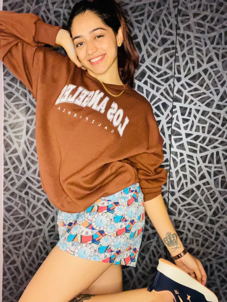 Woman in a brown sweatshirt and Whats Down multicolour printed boxers against a patterned wall smiling