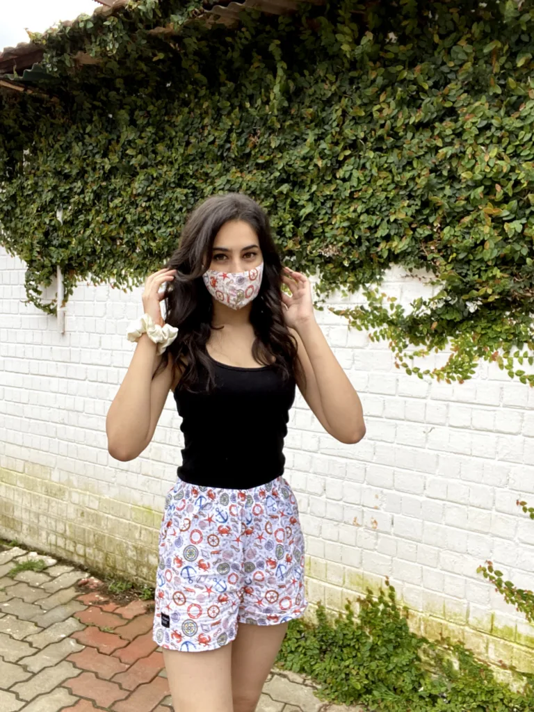 Woman in a Whats Down printed face mask and white floral boxers by an ivy-covered wall
